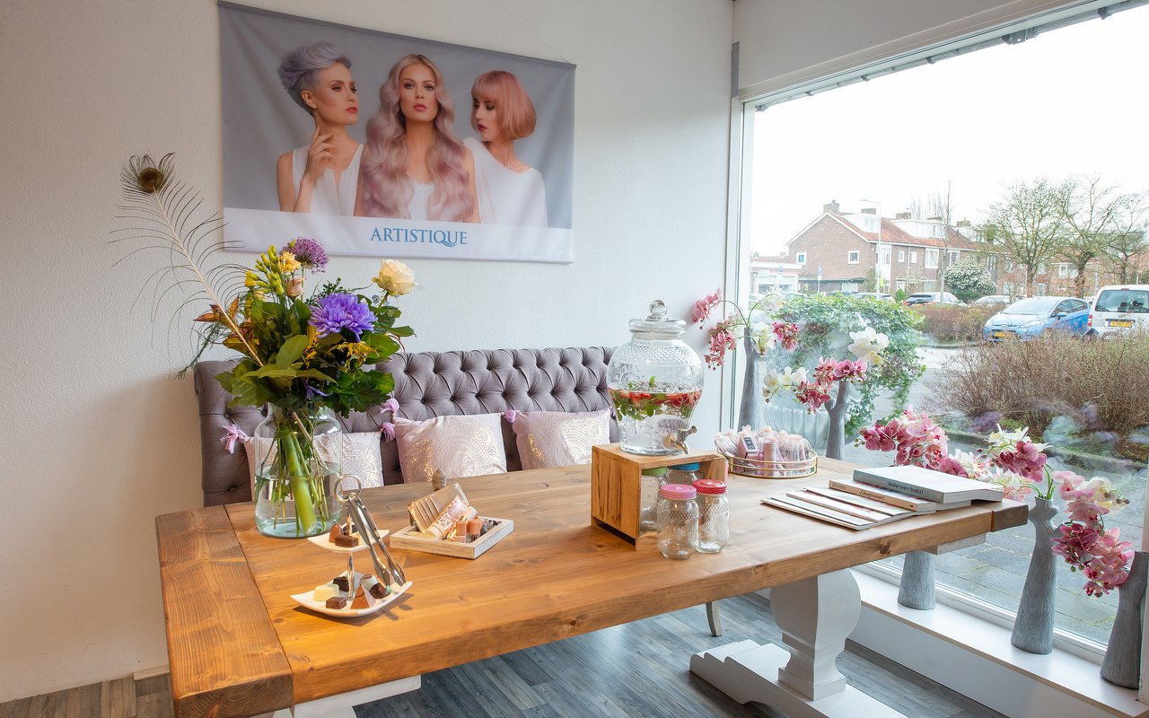 De lounge met de grijze bank, een houten tafel, bloemen en drankjes